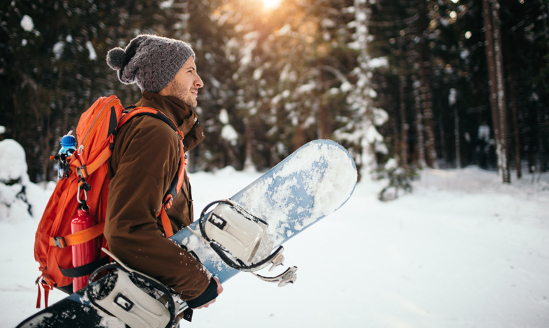 Mężczyzna idący z deską snowboardową w lesie