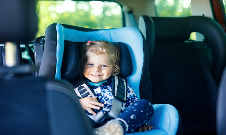 Uśmiechająca się dziewczynka siedząca na tylnim siedzeniu w niebieskim foteliku samochodowym