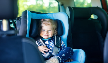 Uśmiechająca się dziewczynka siedząca na tylnim siedzeniu w niebieskim foteliku samochodowym
