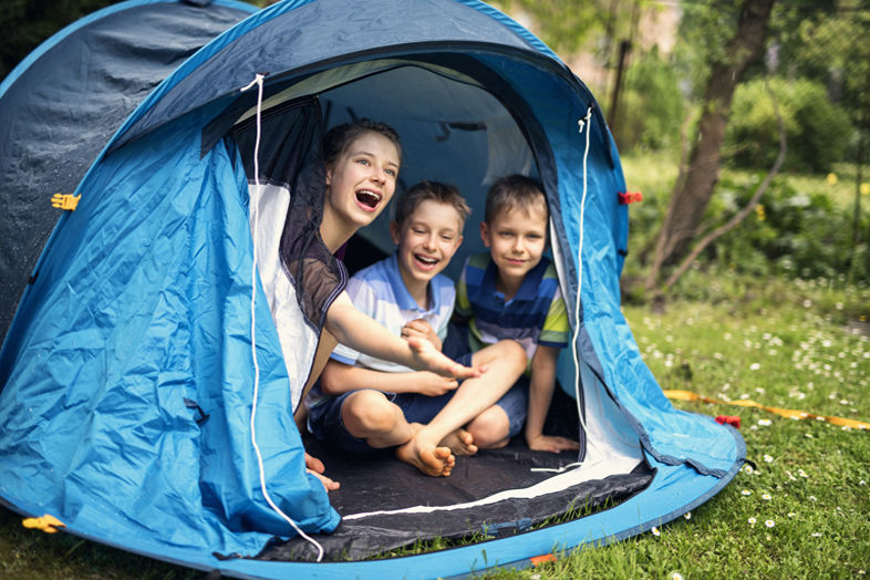 Troje śmiejących się dzieci siedzących w namiocie w ogrodzie w słoneczny dzień