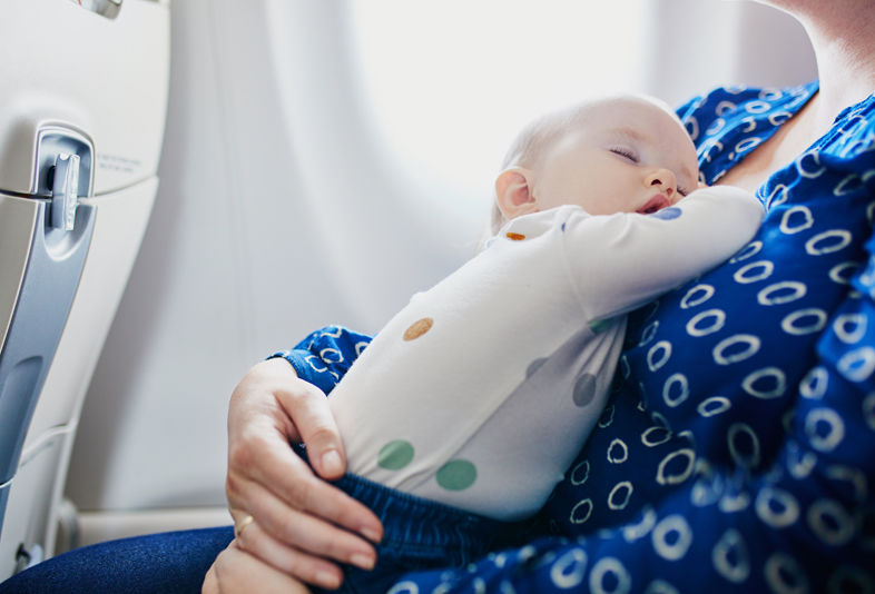Podróżująca kobieta ze śpiącym dzieckiem na rękach w samolocie
