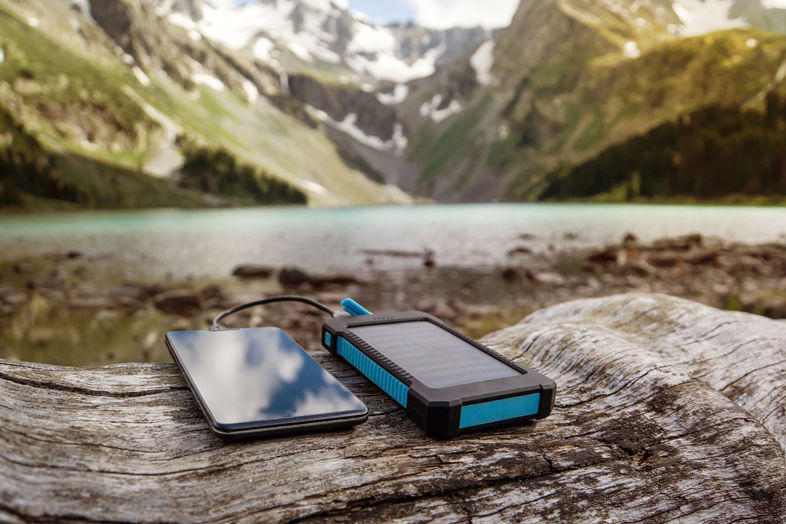 Telefon leżący na kłodzie ładowany urządzeniem na energię słoneczną w górach
