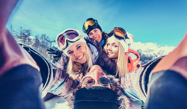 Grupa młodych osób w czapkach i goglach robi sobie selfie w górach