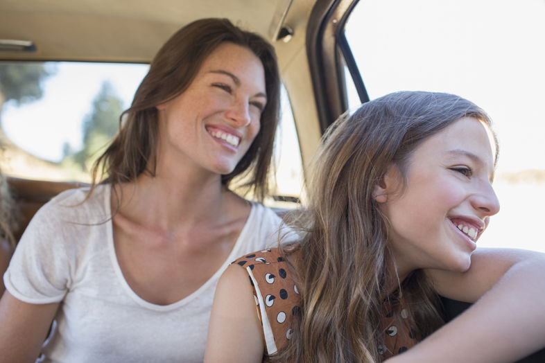 Uśmiechnięta matka z córką siedzące na tylnich siedzeniach patrzące przez okno samochodu